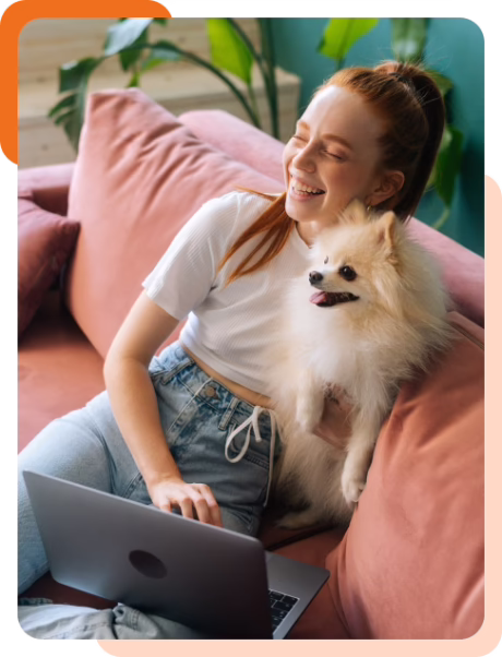 Woman relaxing on a sofa using a laptop with a small dog sitting beside her